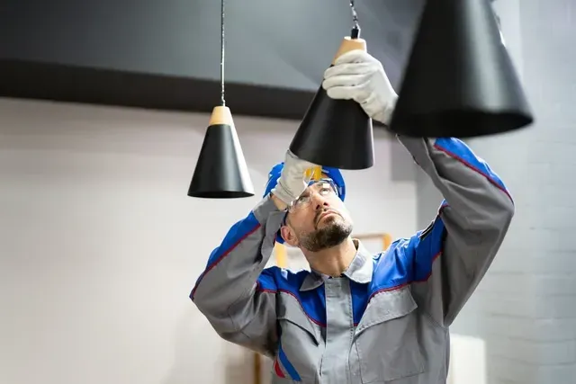 Un homme installe un luminaire au plafond.