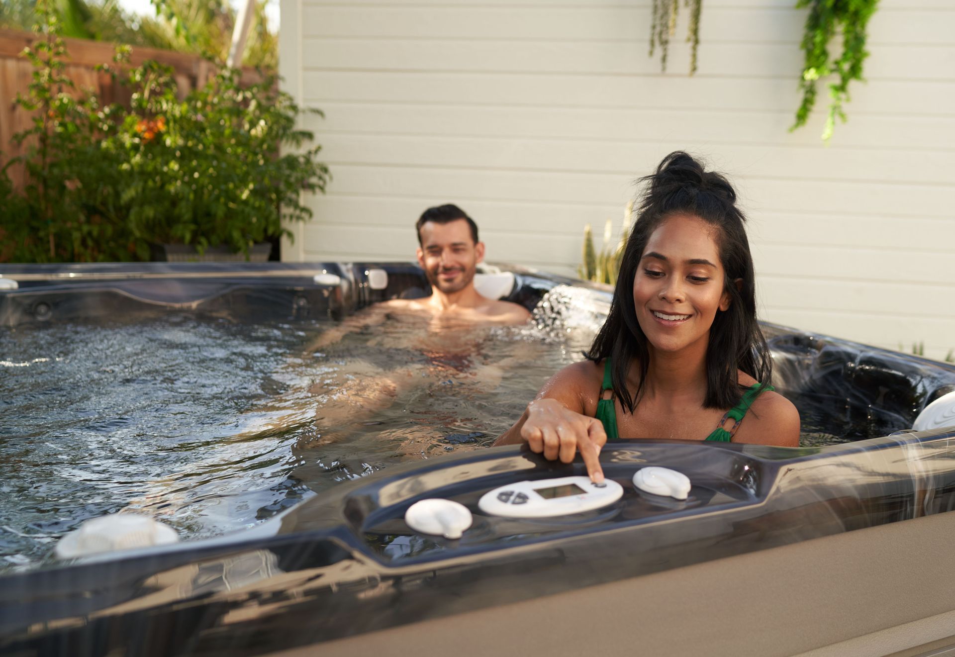 Two people relaxing in a hot tub, smiling, with greenery in the background.