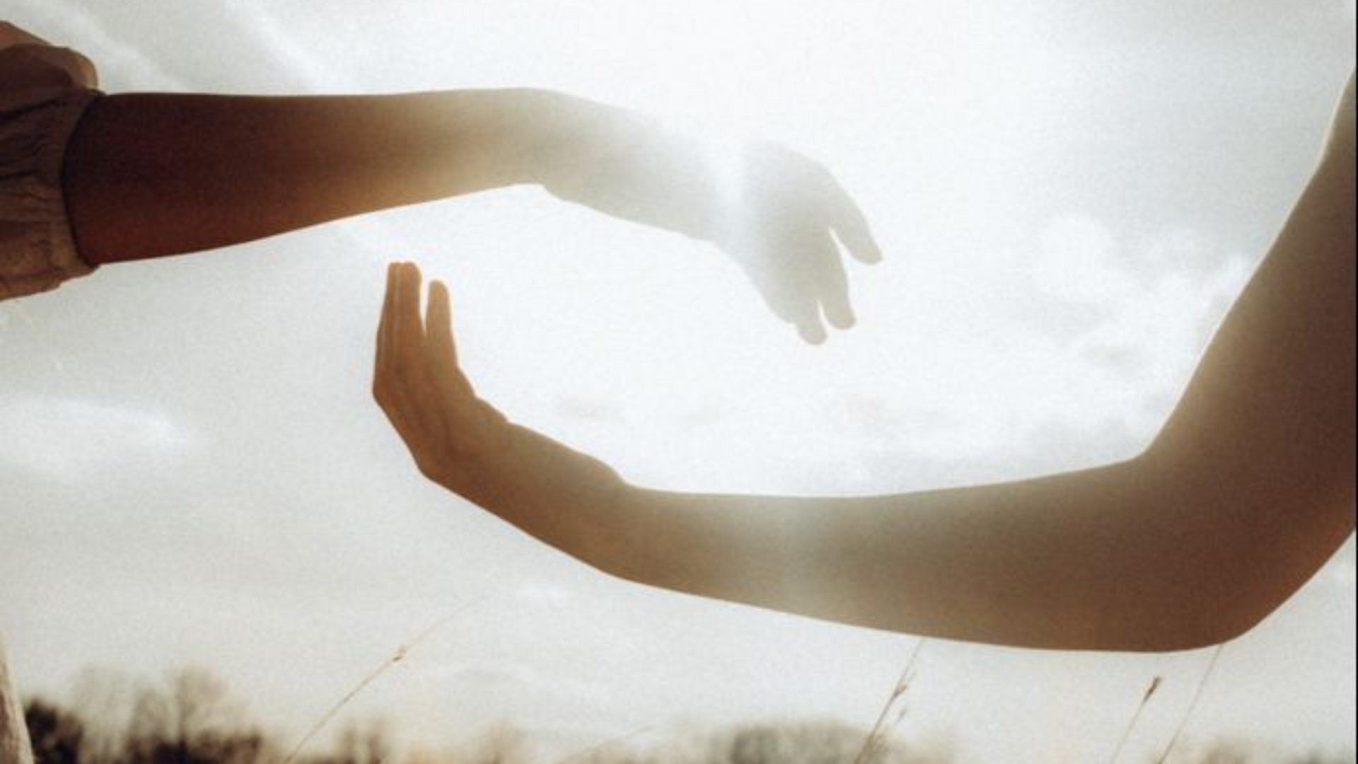 Two arms reaching toward each other in bright backlight at sunset