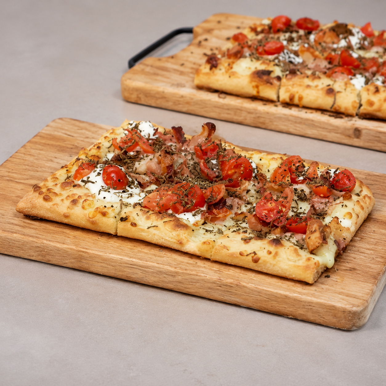 Due pizze rettangolari su taglieri di legno, condite con pomodori ed erbe aromatiche.