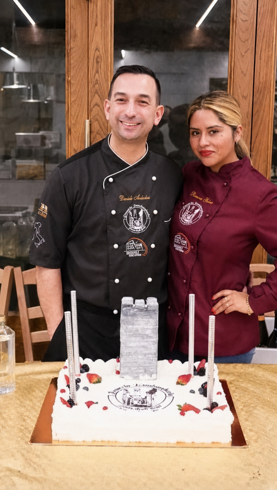 Two people posing behind a birthday cake with lit candles in a restaurant