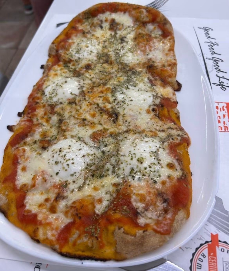 Pizza rettangolare al formaggio su un vassoio bianco, condita con erbe aromatiche e salsa di pomodoro.