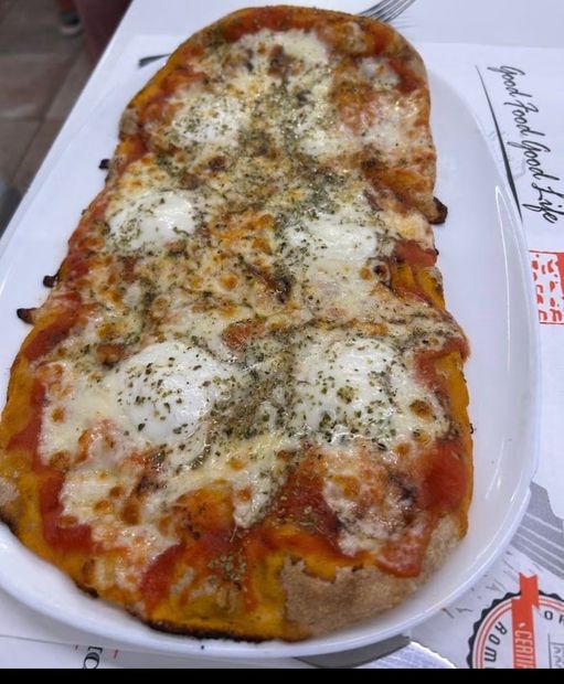 Pizza rettangolare al formaggio con erbe aromatiche su un vassoio bianco, vista dall'alto.