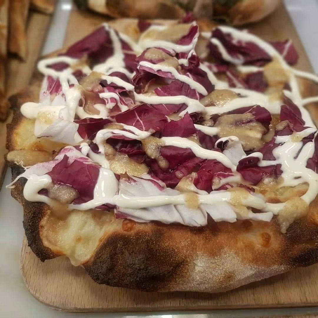 Pizza su pane piatto condita con salsa bianca e cavolo viola, servita su un tagliere di legno.