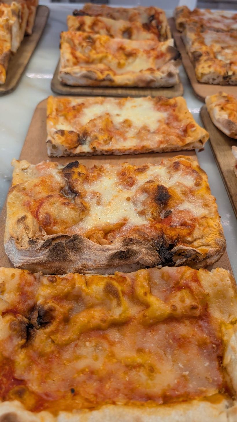 Vassoio di pizze rettangolari cotte al forno con formaggio fuso e salsa, disposte su una superficie metallica.