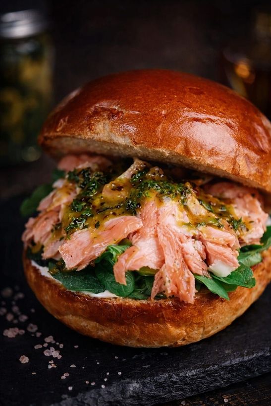 Panino al salmone su un panino brioche lucido con verdure, su una superficie di ardesia scura