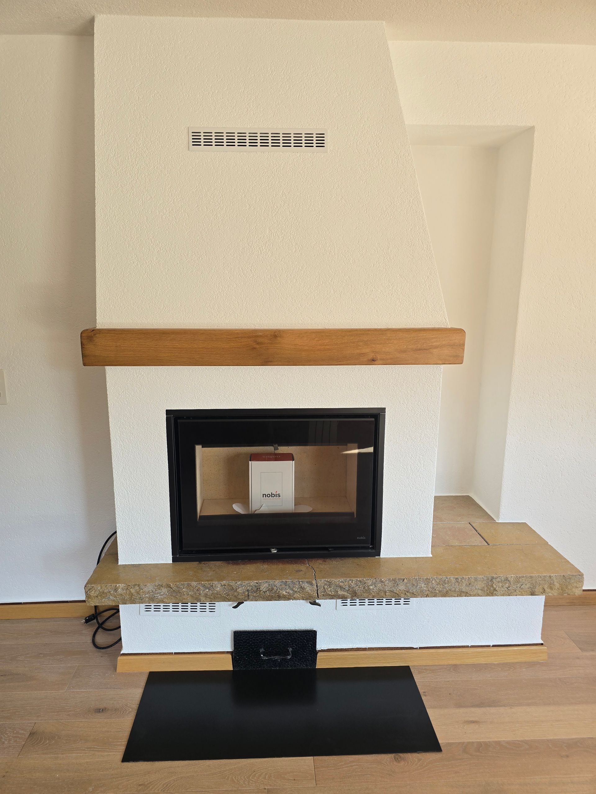 Cheminée blanche moderne avec manteau en bois et foyer noir, posée sur un petit tapis de cheminée noir.