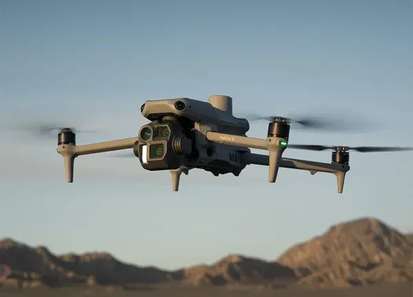 Un drone gris survole les montagnes désertiques sous un ciel dégagé.