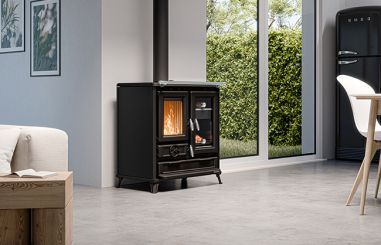 Salon moderne avec un poêle à bois noir allumé près de grandes fenêtres et un canapé clair