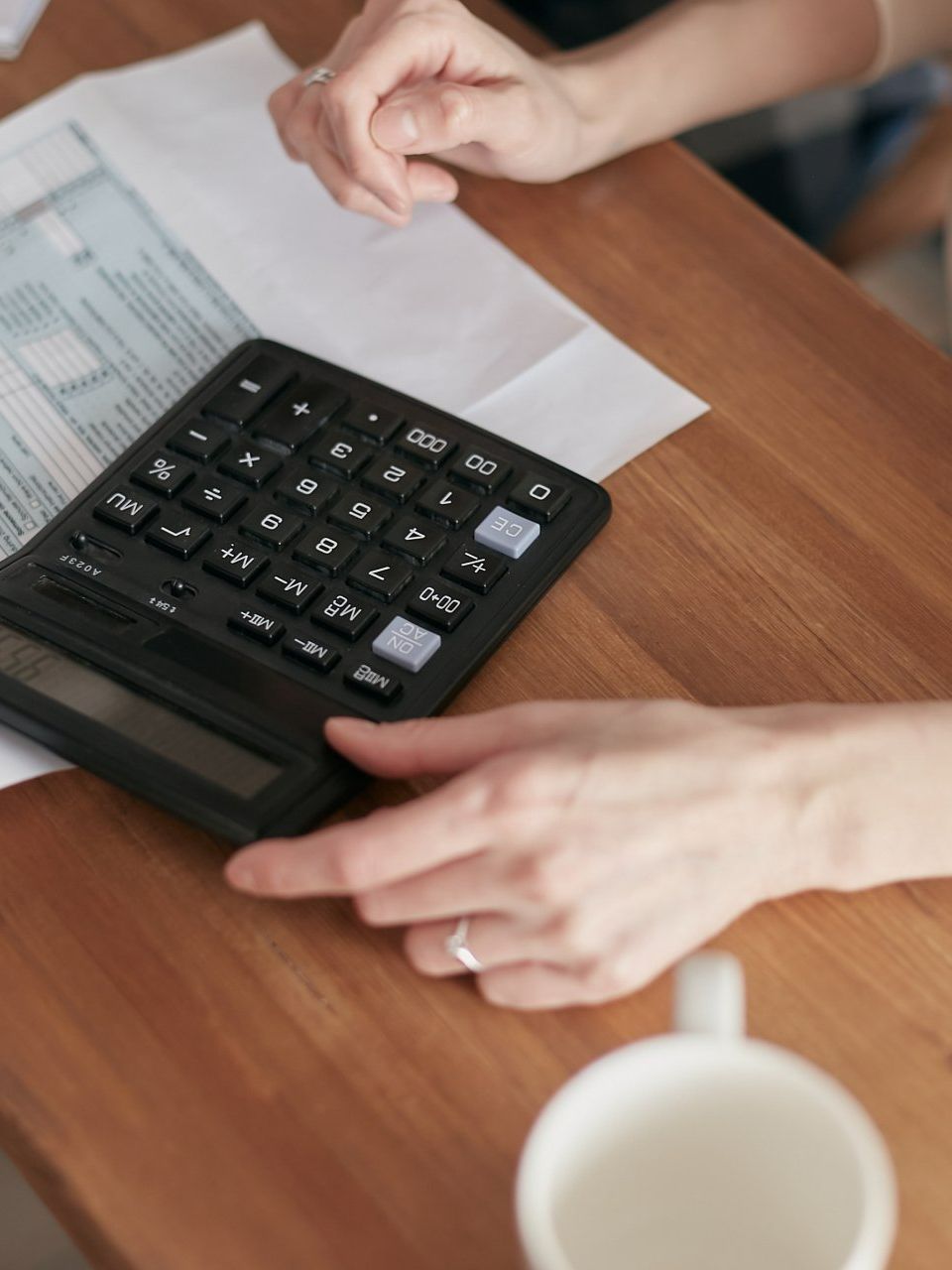 A person is using a calculator on a wooden table