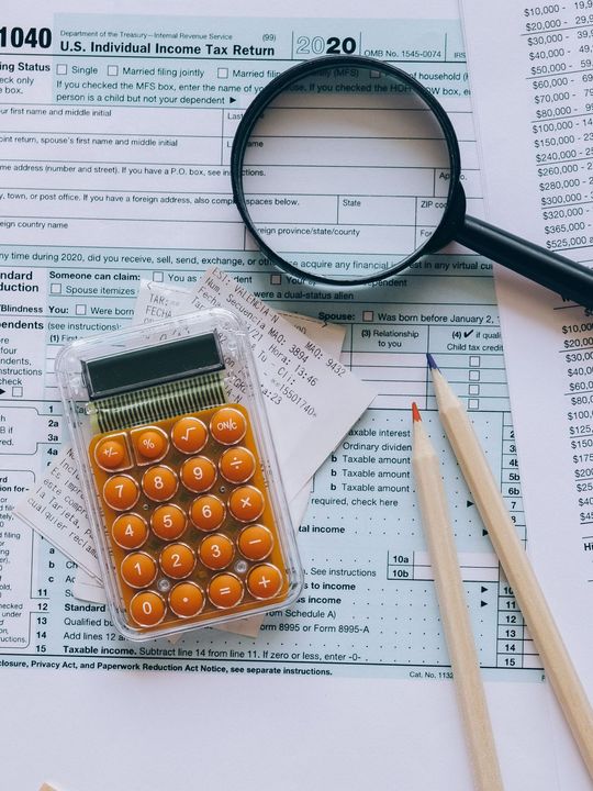 A calculator , magnifying glass , and pencils are on top of a tax form.