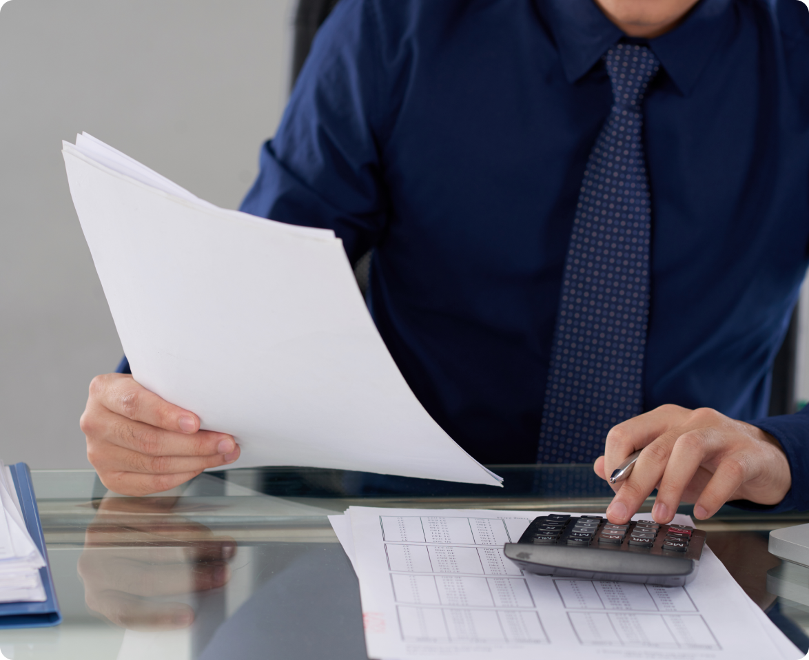 A man in a blue shirt and tie is using a calculator while holding a piece of paper