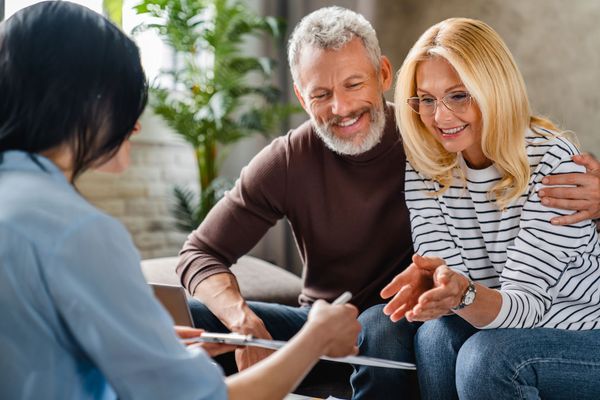 Woman showing document to a smiling couple in a living room; the man has his arm around the woman.
