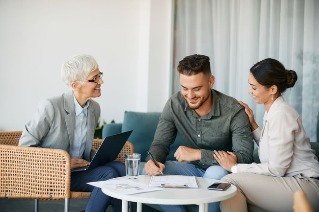 A couple signs paperwork at a table with a professional advisor in a well-lit, modern room.