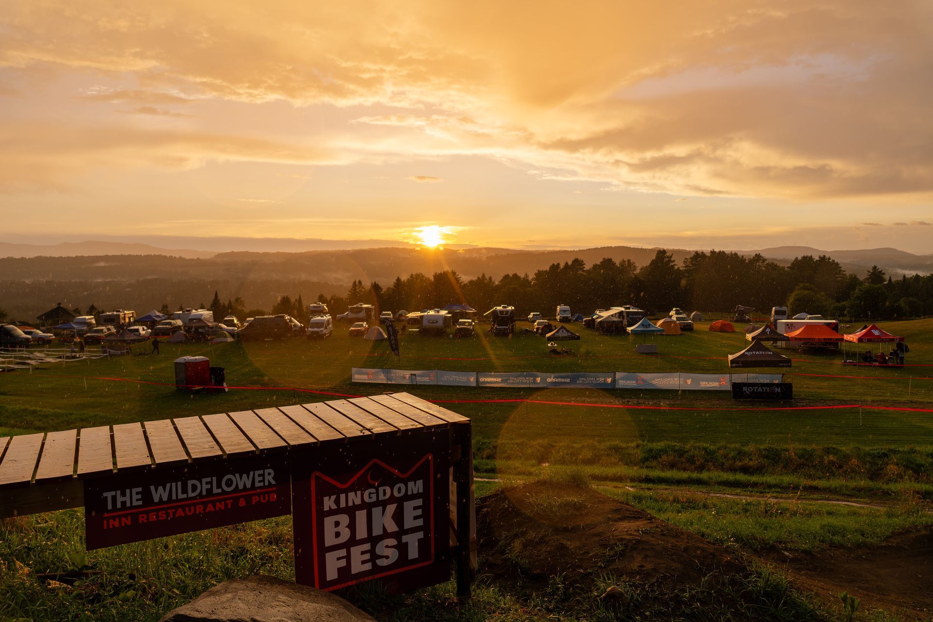 Sunset over a grassy bike festival field with tents and a Wildflower Bike Fest sign in the foreground