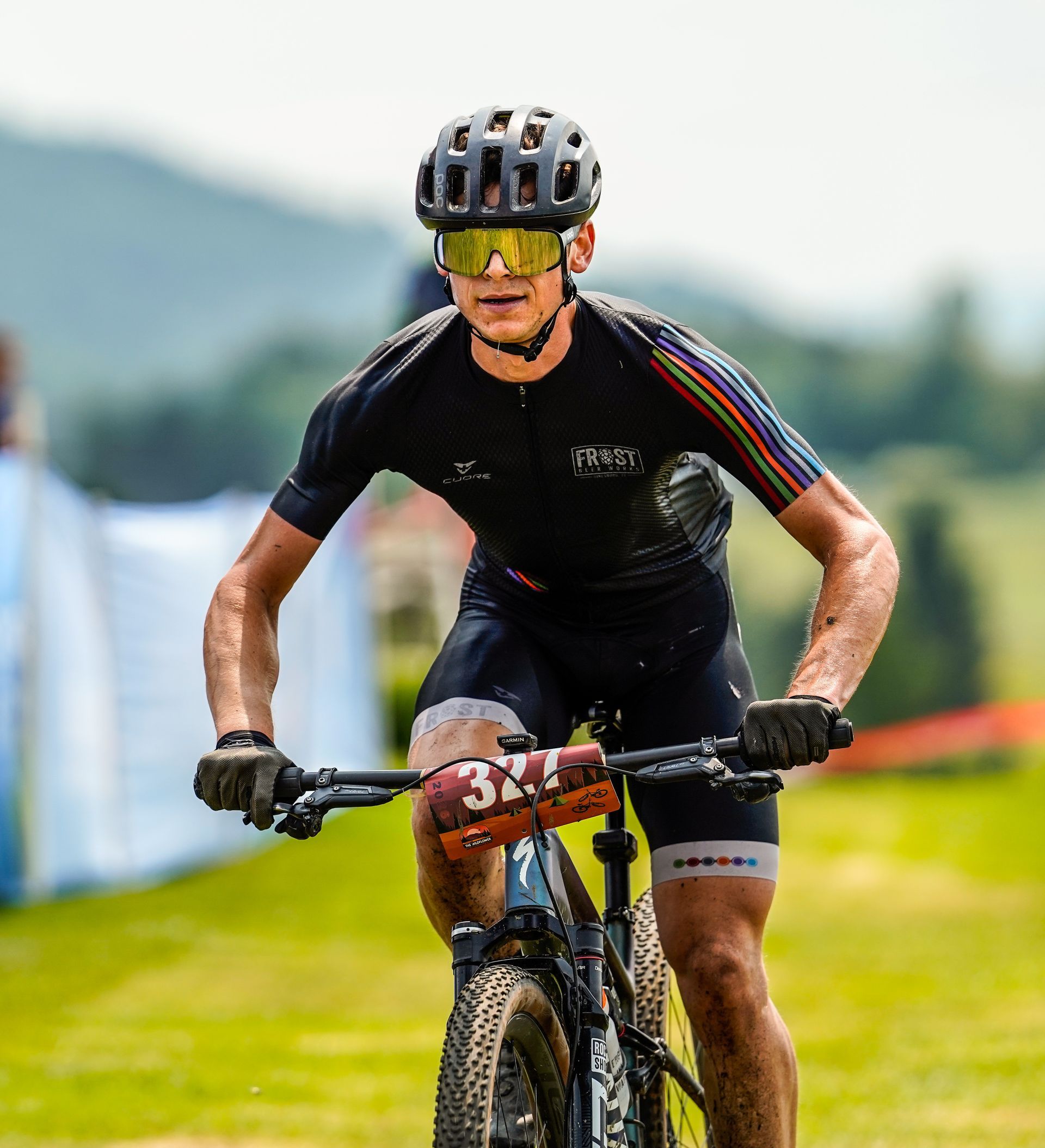 Cyclist in black kit riding on a grassy course, wearing a helmet and yellow sunglasses, race setting