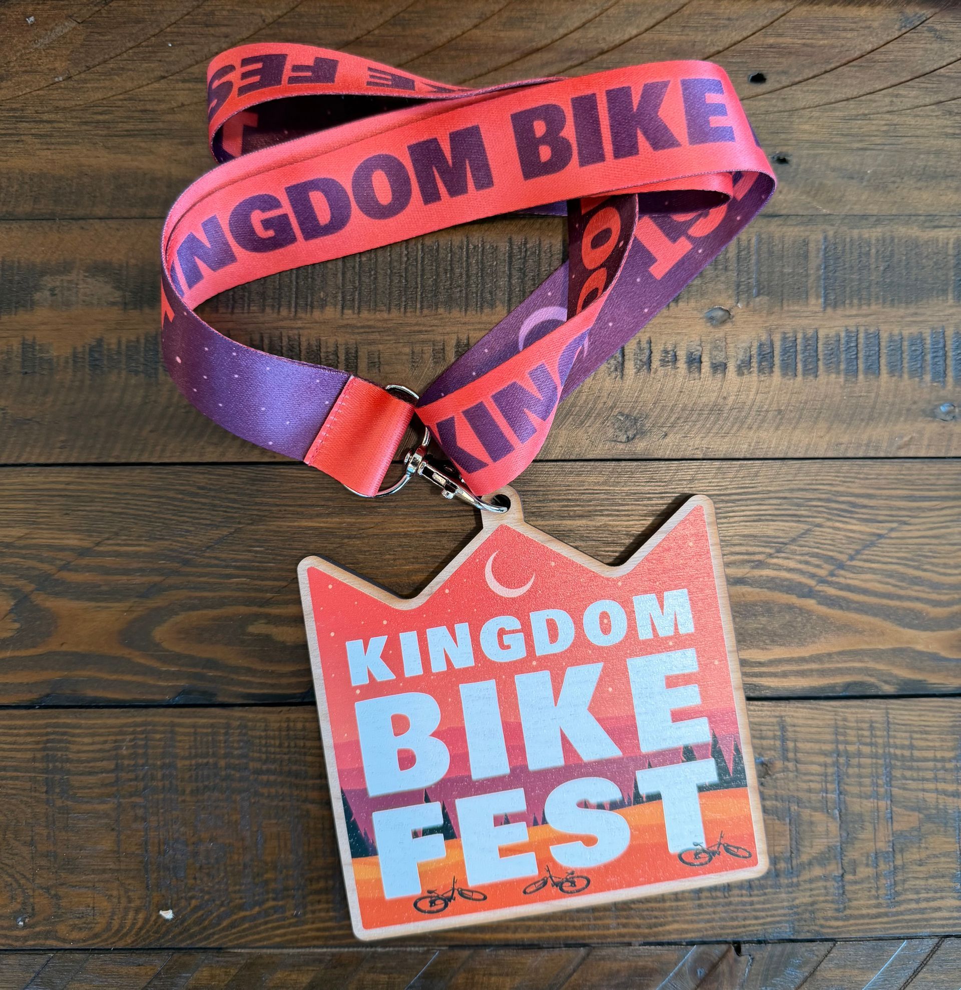 Kingdom Bike Fest lanyard with red-orange badge on a wooden surface
