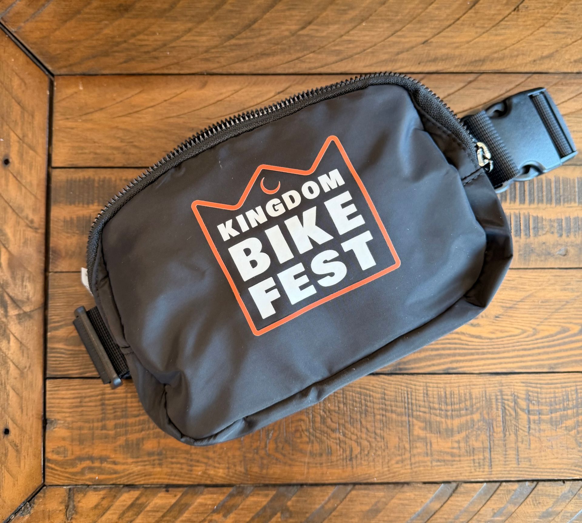 Black bike seat bag with “Kingdom Bike Fest” logo on a wooden floor.