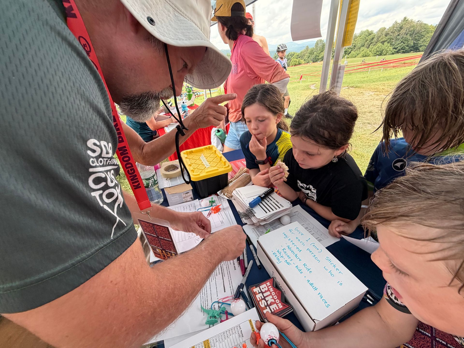 People gathered around a table outdoors, filling out forms and using a tablet during an activity.