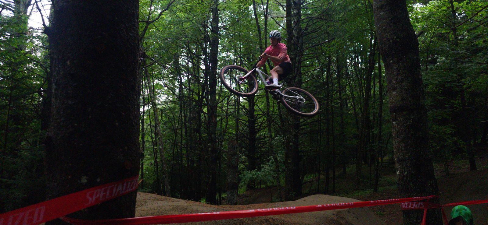 Mountain biker airborne over a red ramp in a forest trail