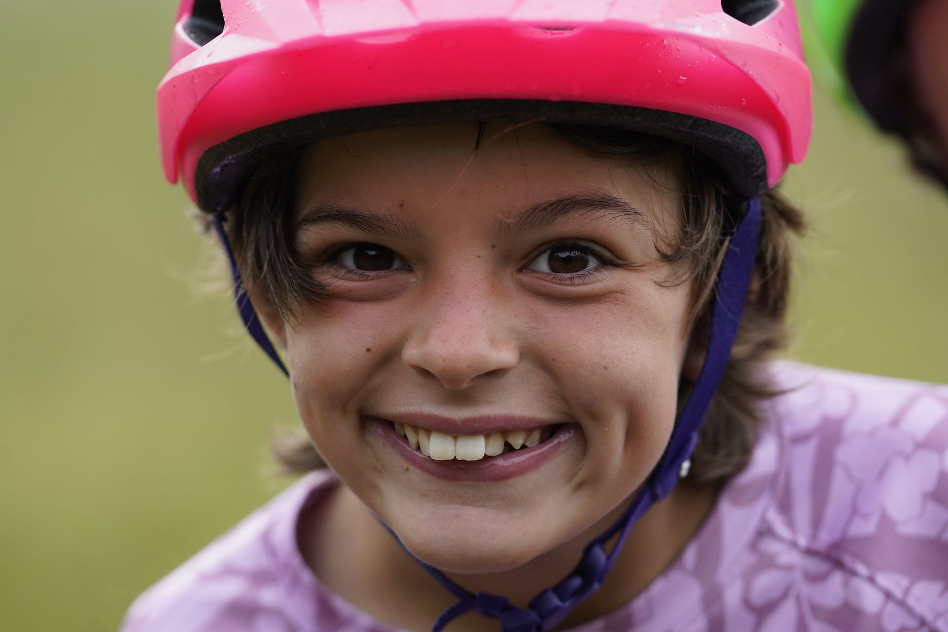 Smiling child wearing a pink helmet and purple shirt outdoors