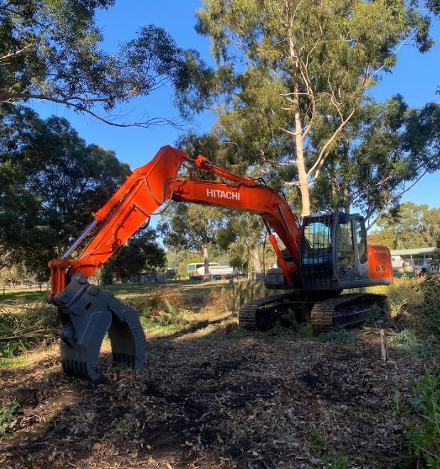 A hitachi excavator is parked in a field with trees in the background