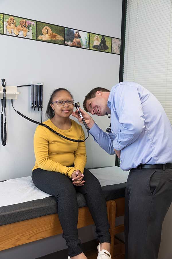 Doctor examining a seated patient with an otoscope in a clinic room