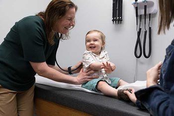 Doctor examining a smiling child on an exam table in a clinic room