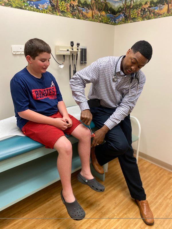 Doctor examining a seated boy’s leg in a clinic exam room