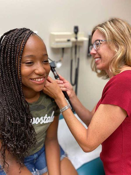 Healthcare worker using an otoscope to examine a smiling patient in a clinic exam room