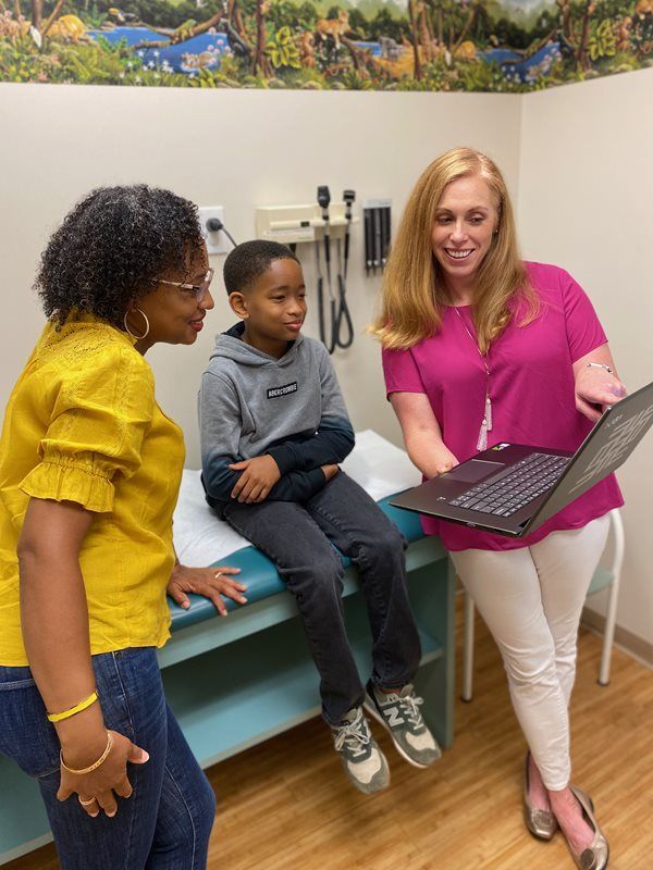 Clinician shows laptop to two children in a medical exam room