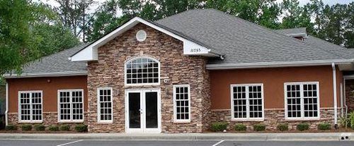 Brick building with arched central entrance and white-trimmed windows under a gray shingled roof