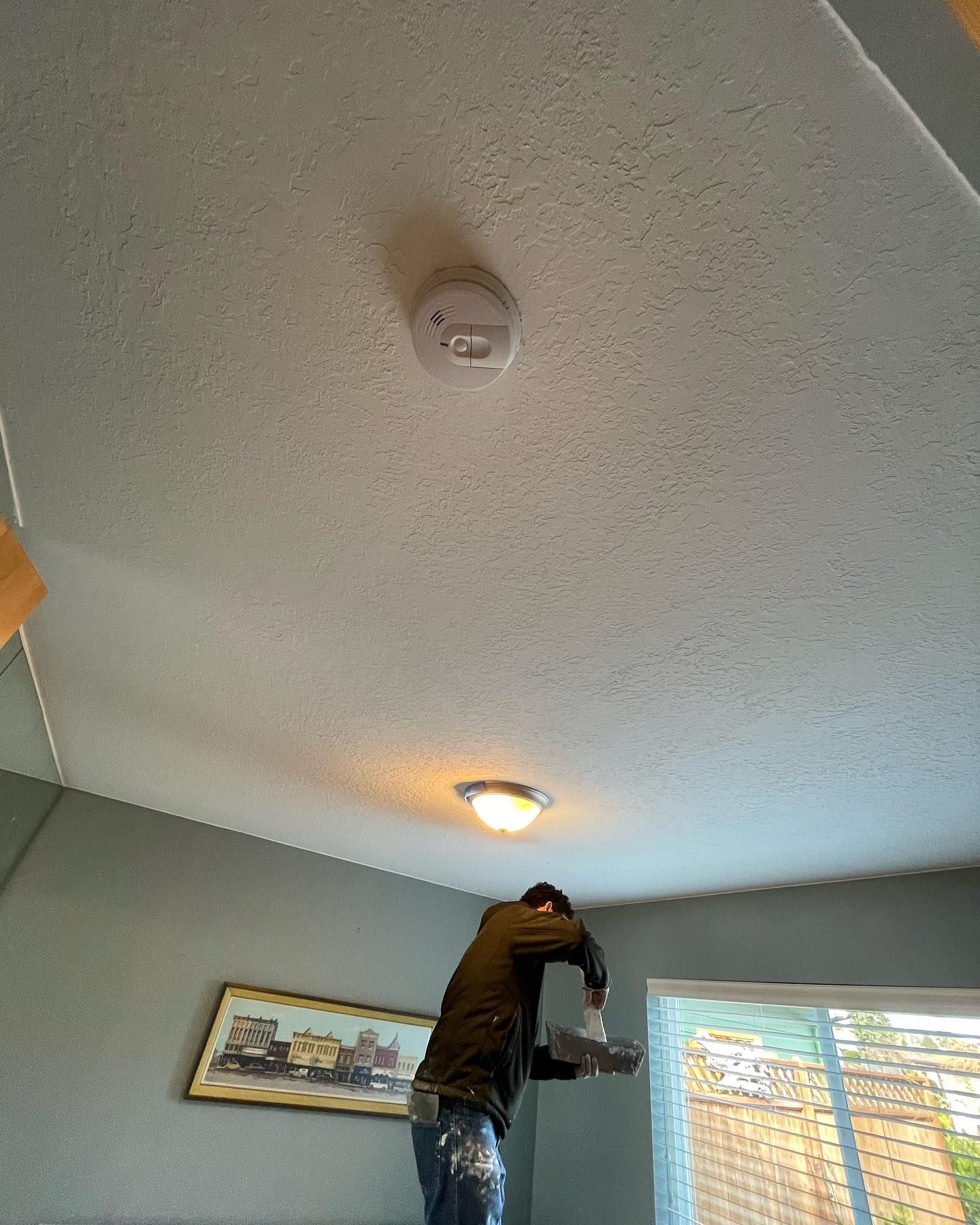 Person on a ladder painting a ceiling with a roller