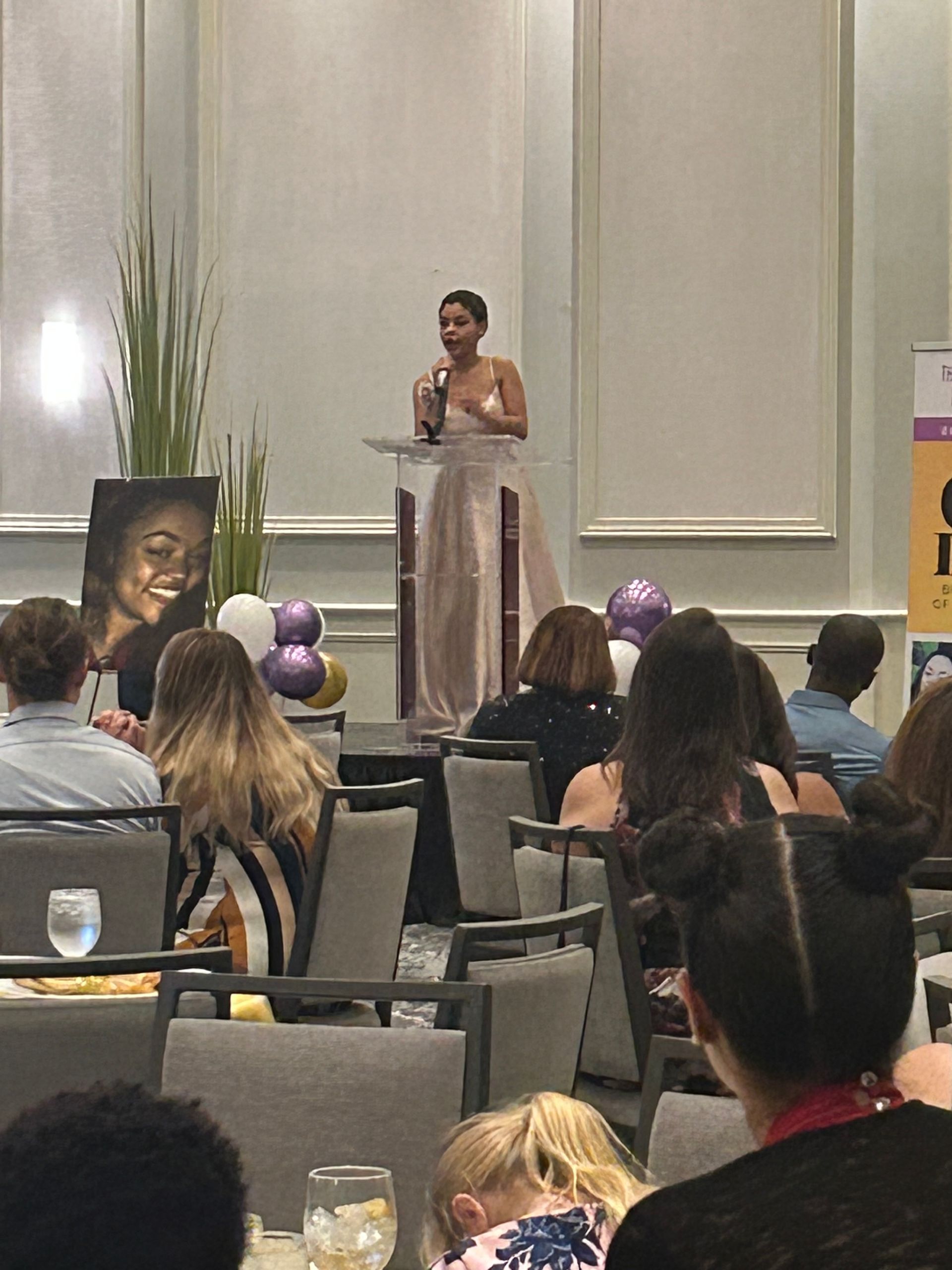 A woman is standing at a podium giving a speech to a crowd of people.