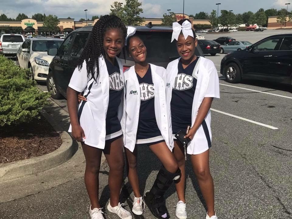 Three cheerleaders are posing for a picture in a parking lot.