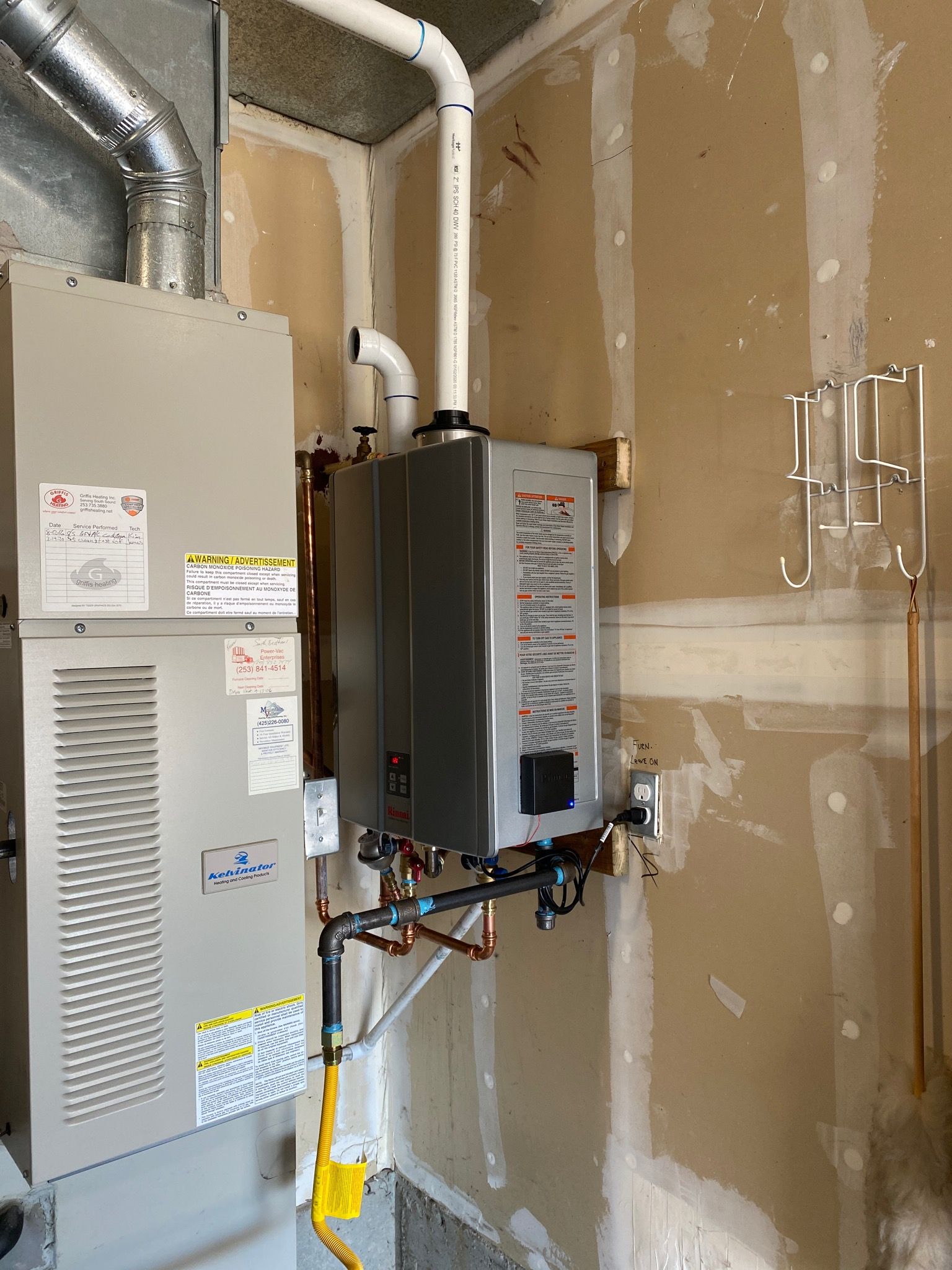 A water heater and furnace unit installed on a wall with exposed drywall. Pipes are visible.