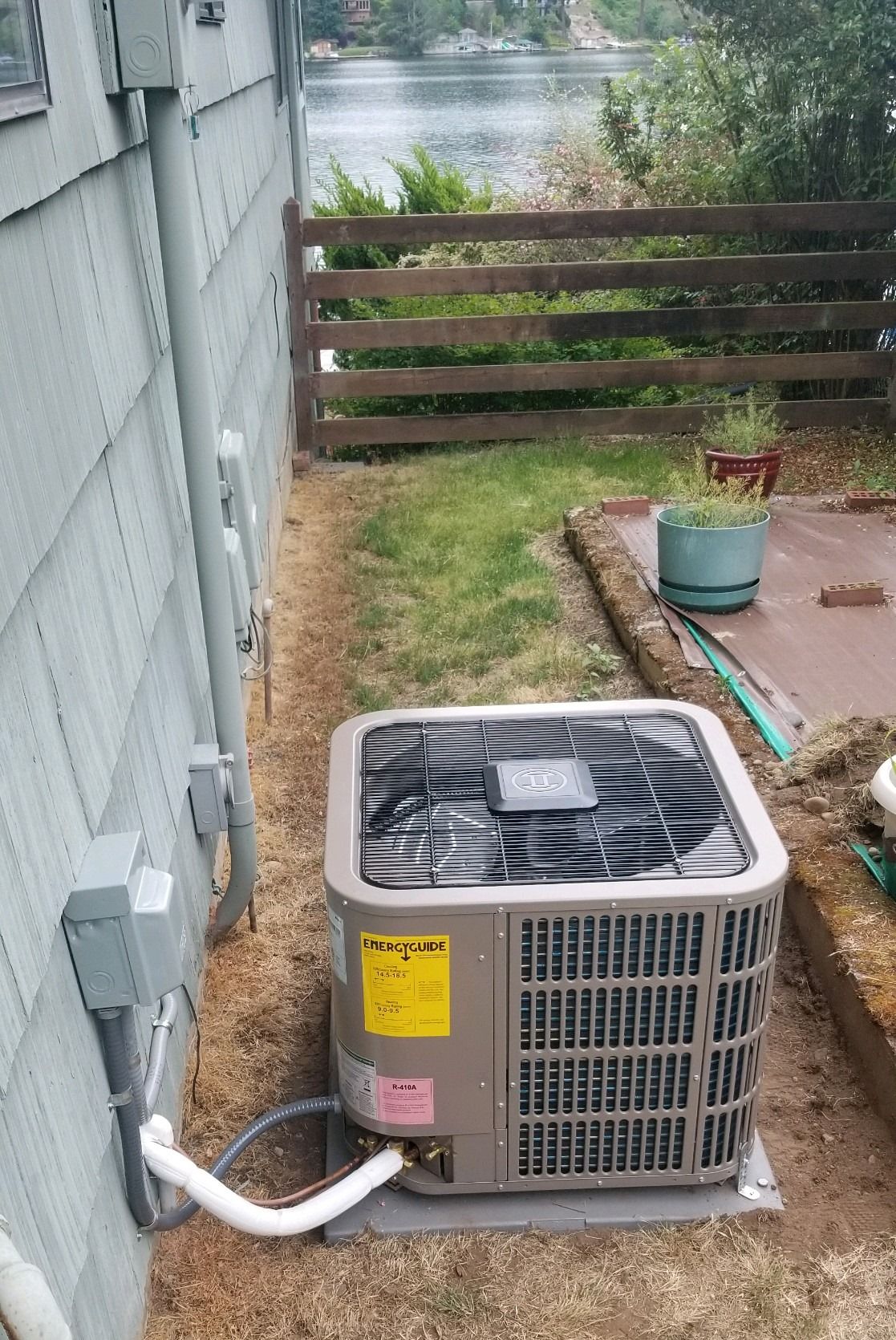 An air conditioning unit next to a house with electrical components and a small yard.