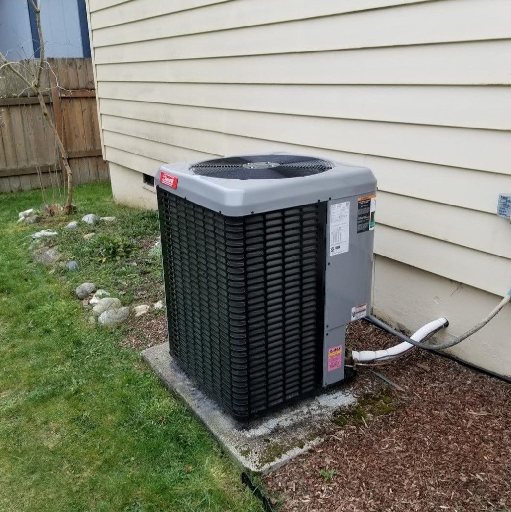 An air conditioning unit next to a light-colored building with green grass and brown mulch.