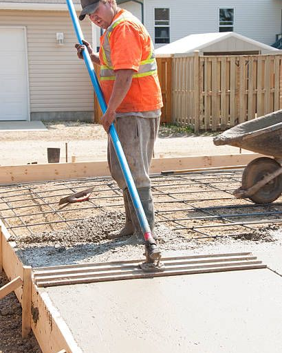 Worker smoothing wet concrete with a long handle tool at a construction site.