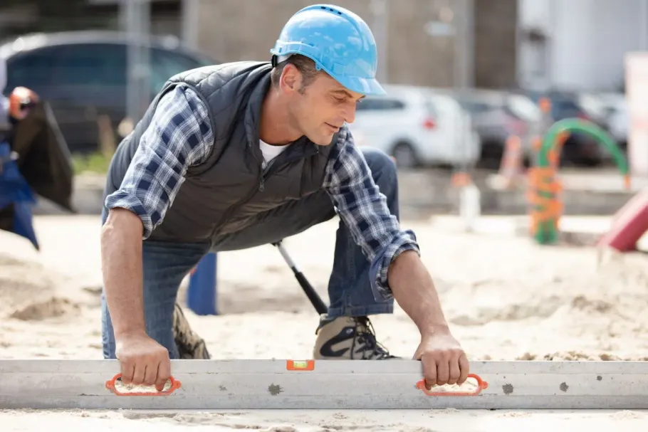 Construction worker in blue hard hat pushing a concrete block at a job site.