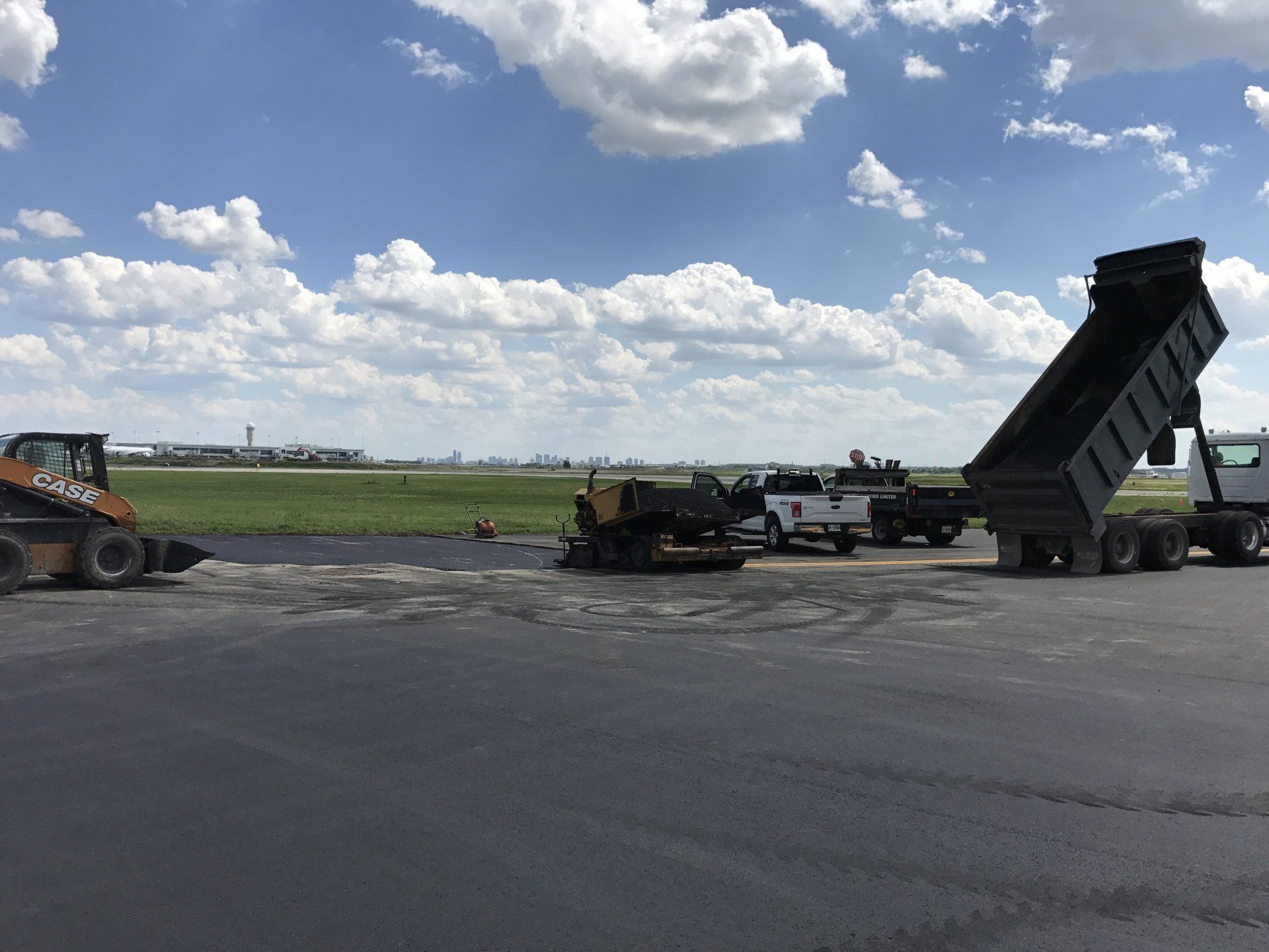 A dump truck is being loaded with asphalt on a construction site.