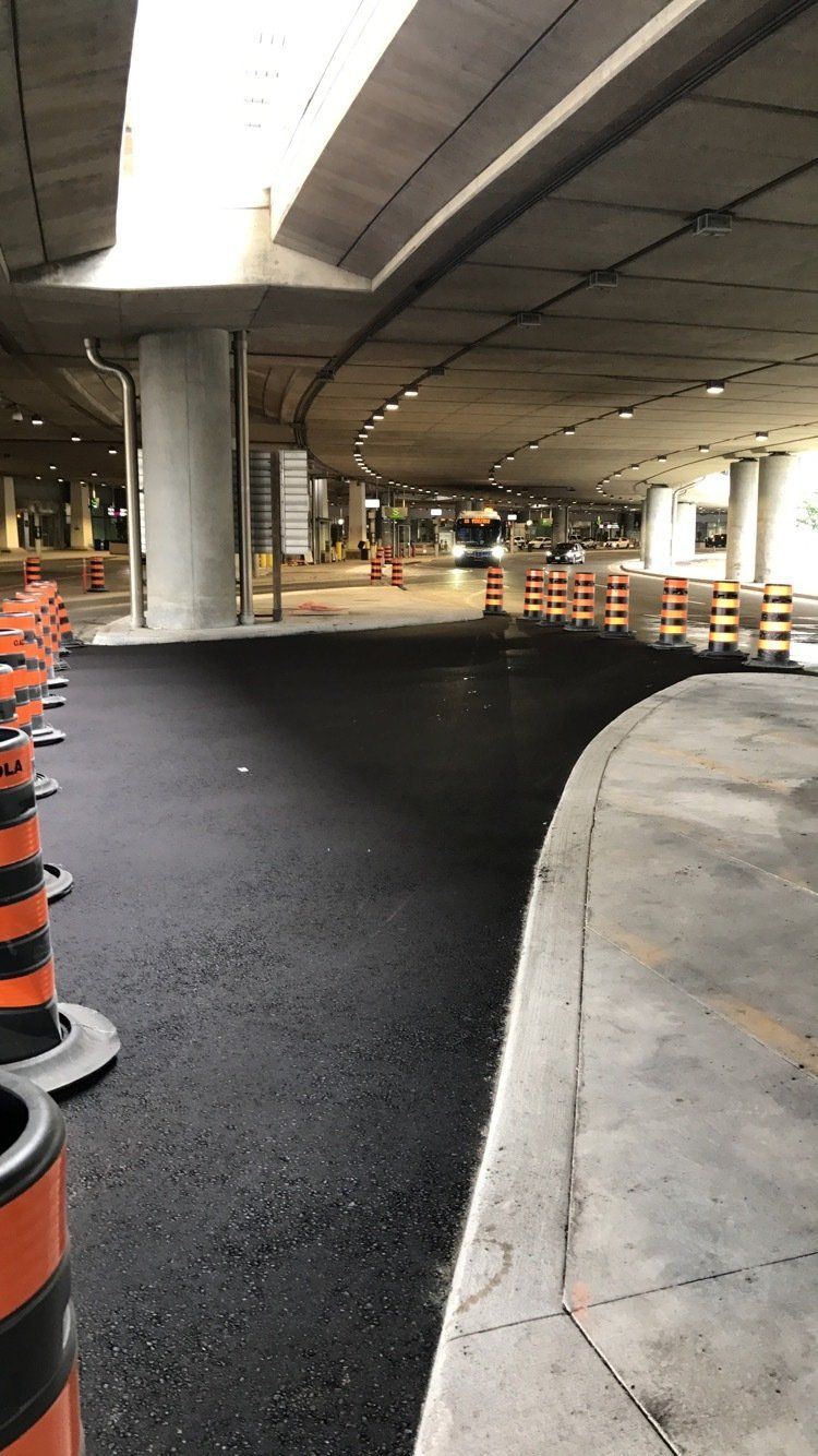 A row of orange and black traffic cones are lined up on the side of a road under a bridge.