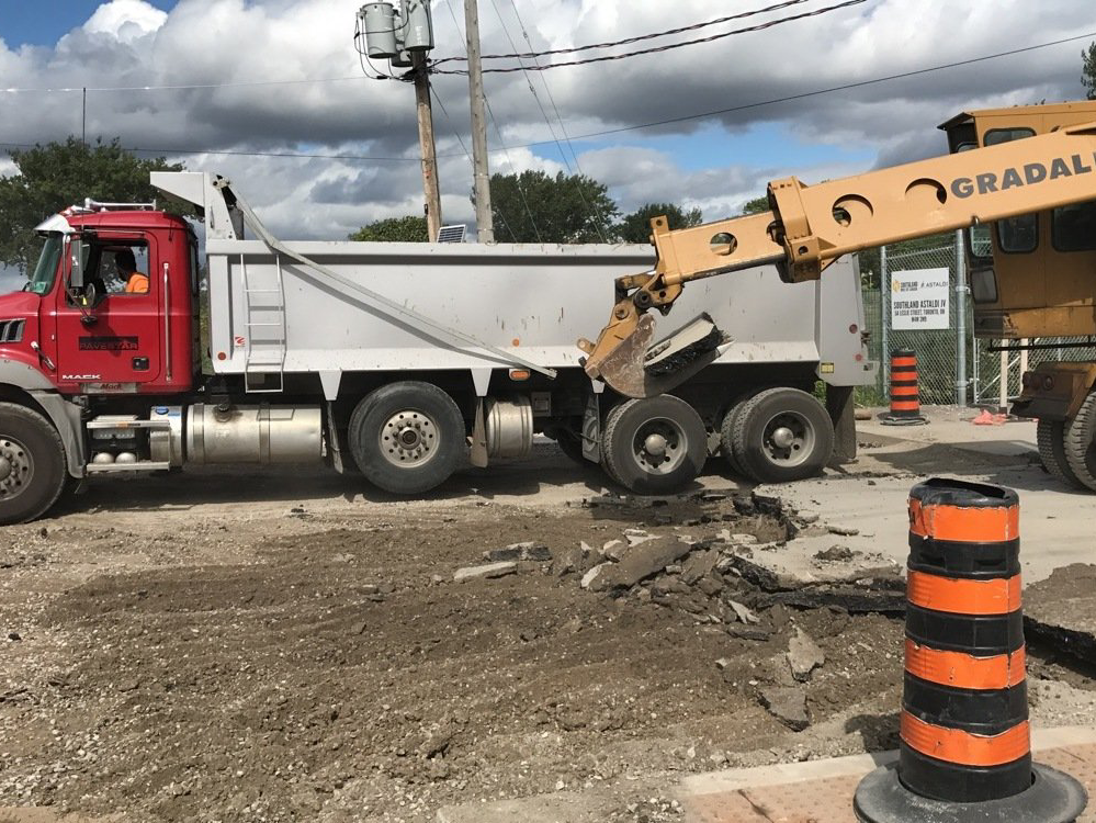 A dump truck is parked on the side of the road next to a crane.