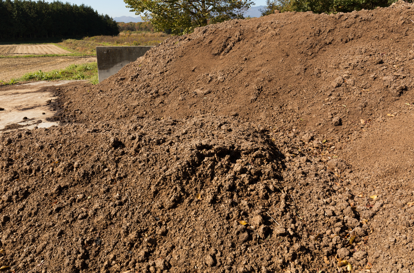 A large pile of dark, loamy soil sitting in an open field under a clear blue sky.