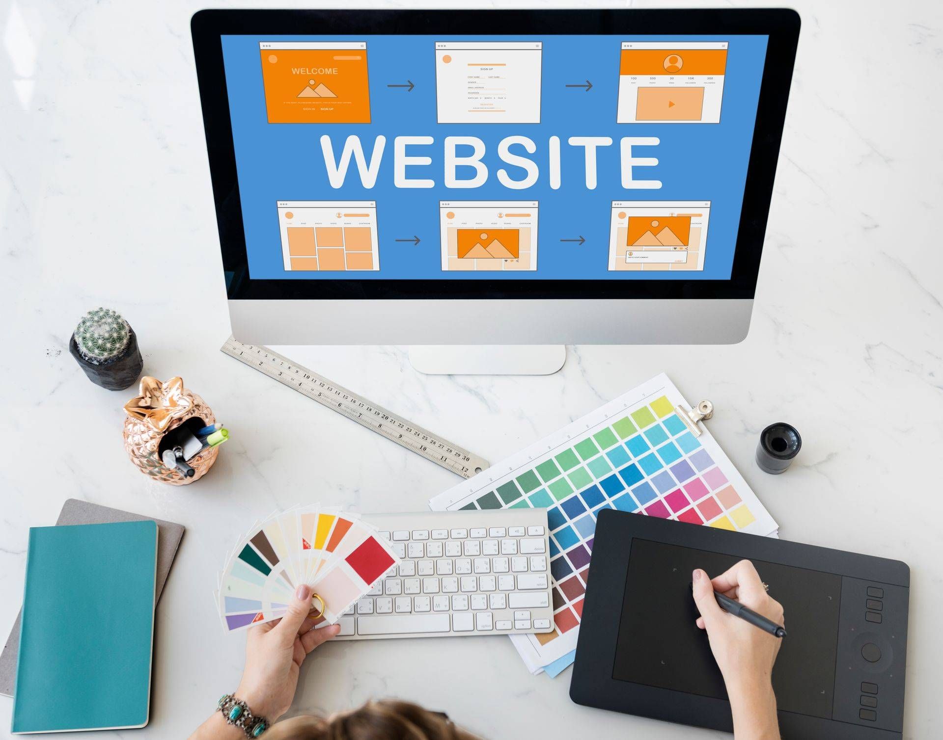 Website design workspace with desktop monitor, color swatches, keyboard, tablet, and tools on a desk