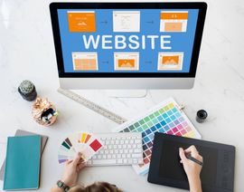 Website design workspace with desktop monitor, color swatches, keyboard, tablet, and tools on a desk