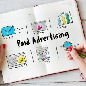 Notebook with “Paid Advertising” sketches, charts, and hands holding a pencil and phone on a desk