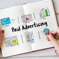 Notebook with “Paid Advertising” sketches, charts, and hands holding a pencil and phone on a desk