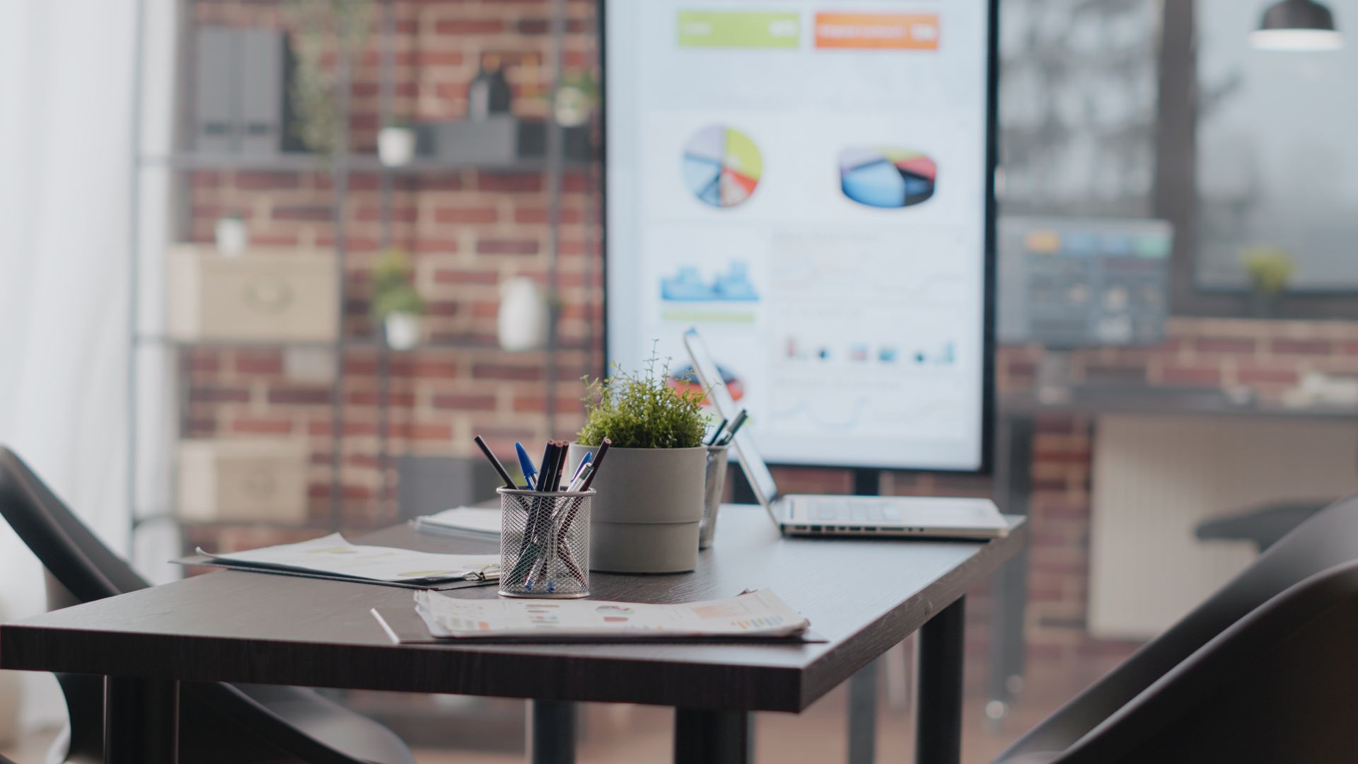 Office meeting room with a table, chairs, laptop, and presentation screen displaying charts