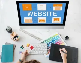 Website design workspace with desktop monitor, color swatches, keyboard, tablet, and tools on a desk